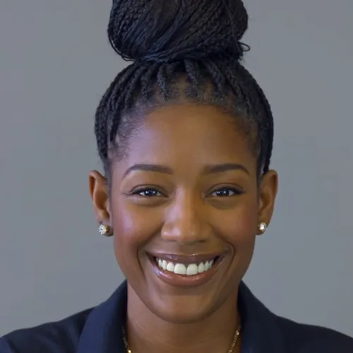 Smiling young woman with braided hair in a bun wearing earrings and a necklace against a gray background