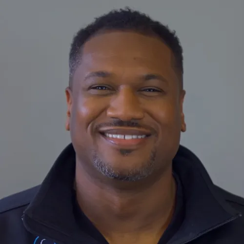 Smiling doctor wearing a white coat and tie, against a gray background.