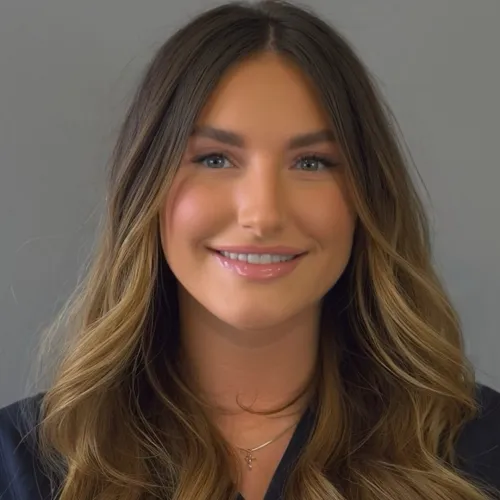 Portrait of a smiling woman with long wavy blonde hair and subtle makeup against a gray background