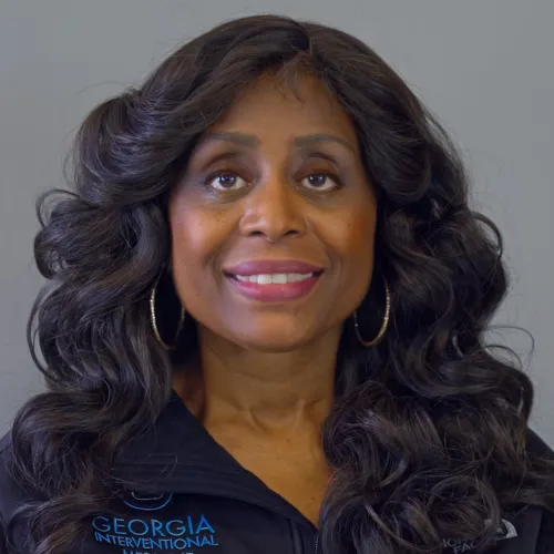 Smiling woman with long curly hair wearing Georgia Interventional Medicine jacket and hoop earrings