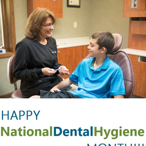 Dental hygienist smiling and showing a dental model to a boy in a clinic celebrating National Dental Hygiene Month.
