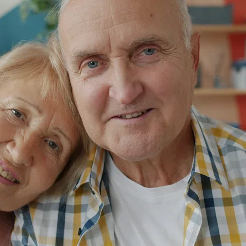 Smiling elderly couple sitting close together in a cozy, colorful living room environment