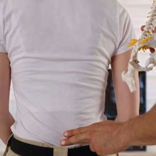 Doctor examining patient's lower back with spine model in medical office, focusing on spine health assessment.