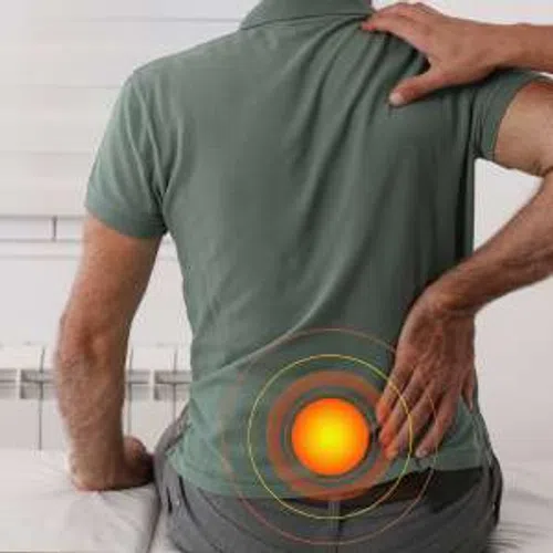 Man in green shirt holding lower back with glowing pain spot highlighted, indicating lower back pain.
