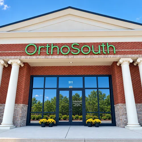 Front entrance of OrthoSouth orthopedic clinic with brick facade, white columns, and green lettering on a sunny day.