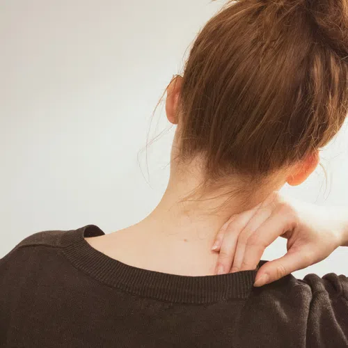 Woman with red hair in a bun scratching her neck wearing a dark sweater against a plain background.