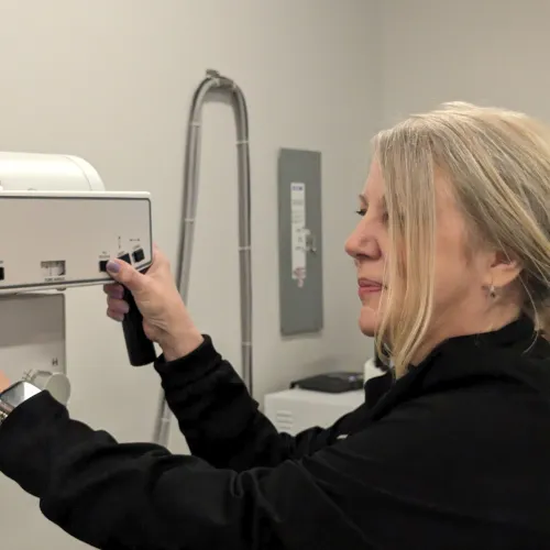 A woman operates medical equipment in a clinical setting, focusing on precision and care.