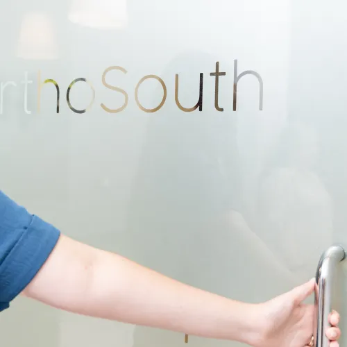 Person opening frosted glass door with OrthoSouth logo in modern medical office environment.