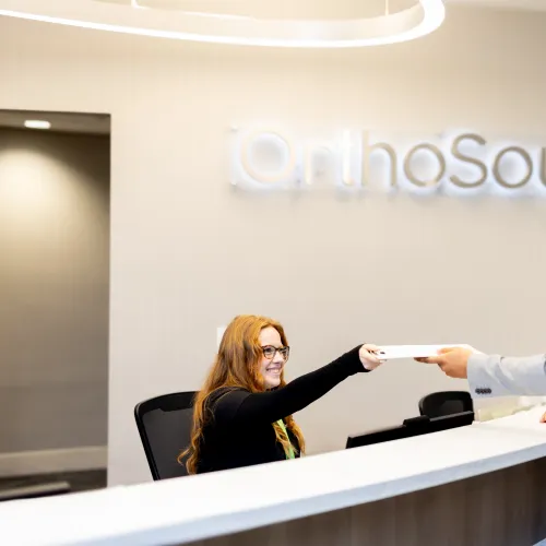 Receptionist handing a document to a client at OrthoSouth office.