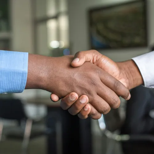 Two diverse hands shaking in a professional office setting, symbolizing partnership and agreement.