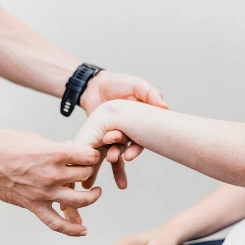 Person examining another person's wrist with hands against a neutral light background.