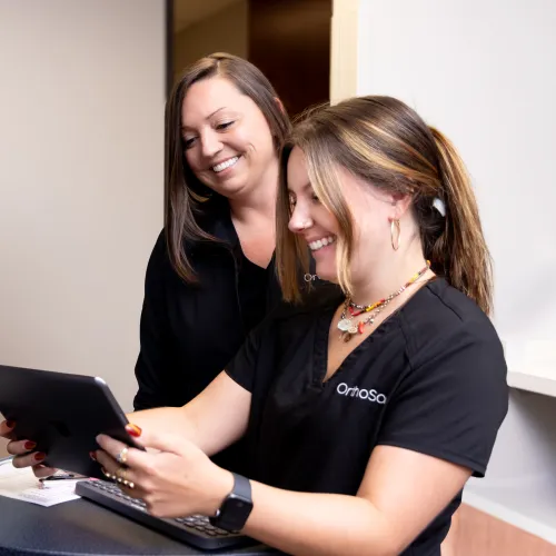 Two healthcare professionals smiling while looking at a tablet in a clinic office setting.