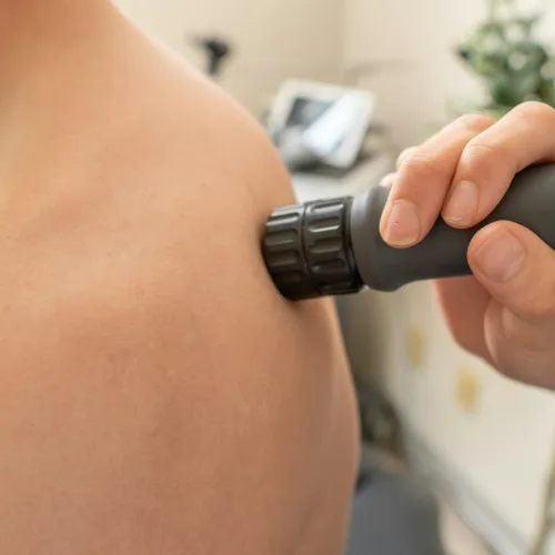 Person receiving shoulder therapy with handheld massage gun for muscle relief and recovery.