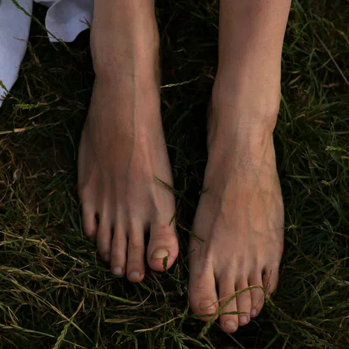 Close-up of two bare feet standing on green grass with some white fabric visible at left edge