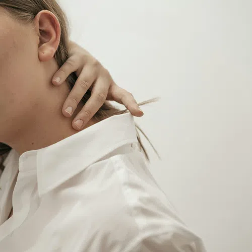 Close-up of a woman in a white shirt touching her neck with a neutral light background