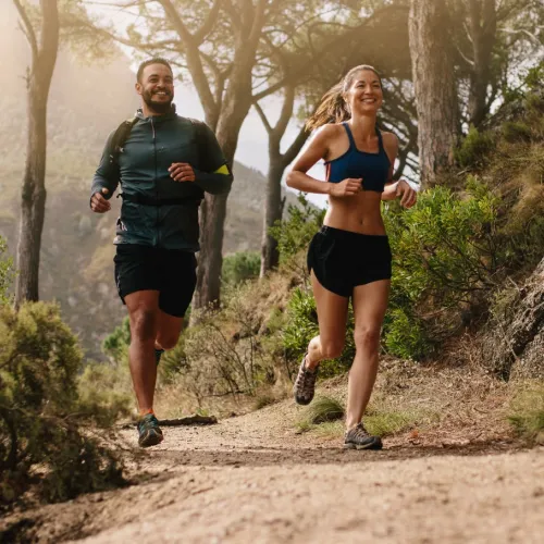 a man and woman running on a dirt path in the woods