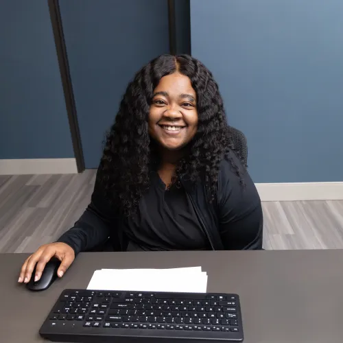 Smiling woman at desk with computer and keyboard in modern office setting.