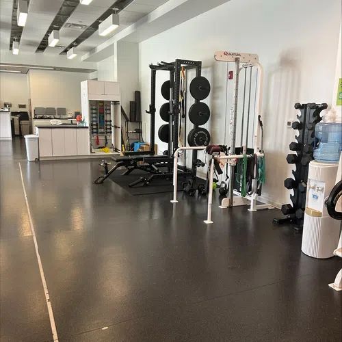 Modern fitness center with weight racks, resistance bands, benches, and a water dispenser in a clean, well-lit space.
