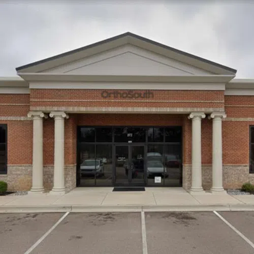 Exterior view of a brick commercial building with columns and glass entrance under a cloudy sky.