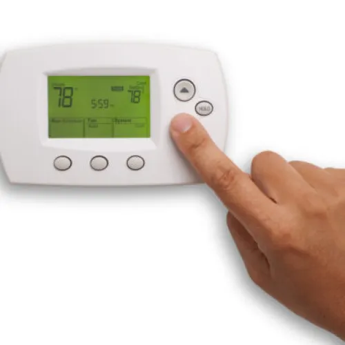 Person adjusting a digital thermostat displaying temperature settings.