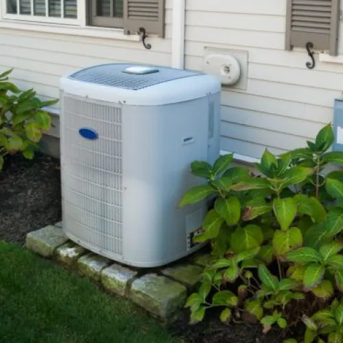 Air conditioning unit installed outside a house surrounded by green plants and stones.