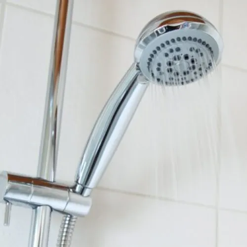 Modern chrome showerhead with water flowing in a bright bathroom setting.