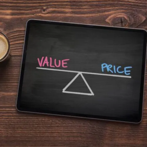 A tablet displaying a balance between value and price, with coffee on a wooden table.