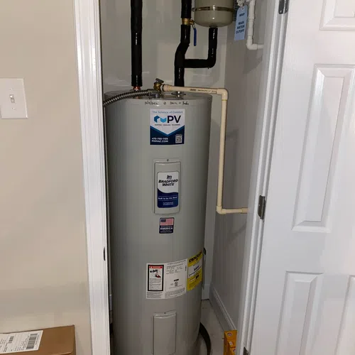 Tall gray Bradford White water heater installed in a small closet with connected black and beige pipes.