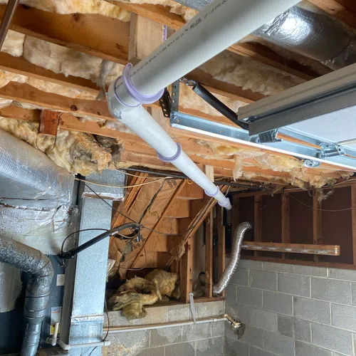 Basement ceiling with exposed wooden beams, insulation, ductwork, and PVC pipe plumbing system.