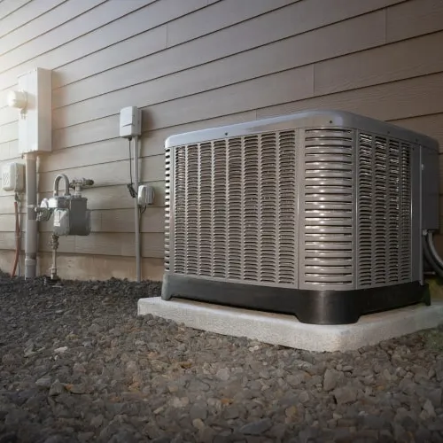Outdoor air conditioning unit installed on concrete slab beside residential house exterior wall during sunset.