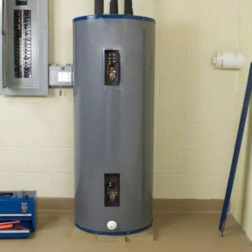 Tall gray water heater installed in basement near electrical panel and blue toolbox on the floor.