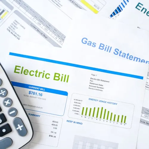 Calculator and multiple utility bills including electric, gas, and energy bills on a white surface.