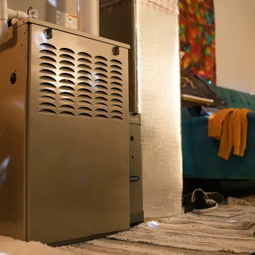 Indoor home furnace unit in a cozy living room with a sofa, rug, and drum set beside it.