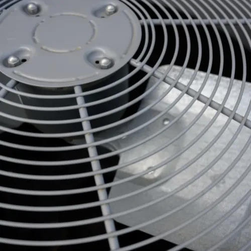 Close-up of a metal fan blade behind a protective circular grill in an air conditioning unit.
