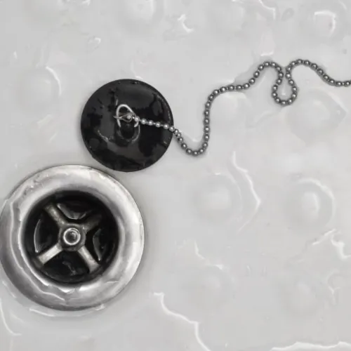 Close-up of a bathtub drain with a metal chain attached to a black rubber stopper on a wet surface.