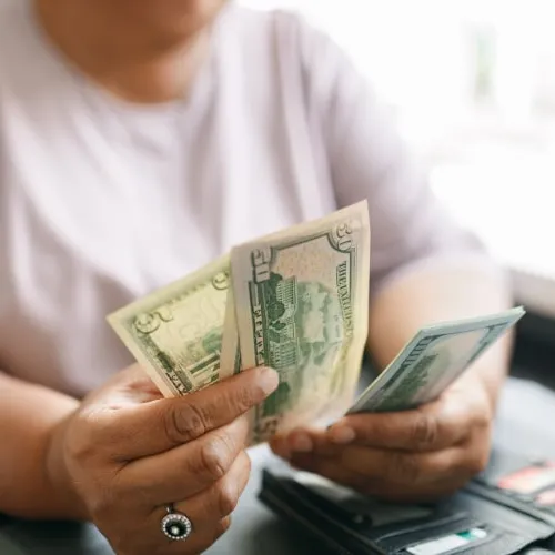 Close-up of a person counting US dollar bills while sitting at a table with a wallet and credit cards.