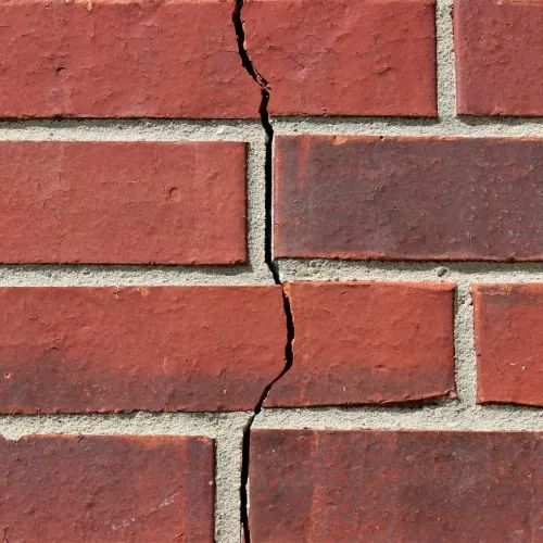 Close-up of a red brick wall with a vertical crack running through the mortar and bricks.