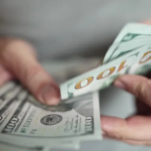 Person counting multiple US 100 dollar bills close-up with blurred background for finance concept