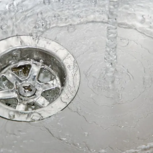Close-up of water flowing into a stainless steel sink drain with visible bubbles and ripples
