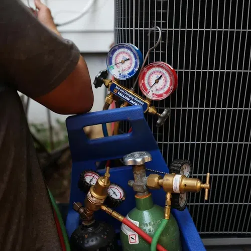 HVAC technician checking refrigerant pressure gauges connected to an air conditioning unit outdoors