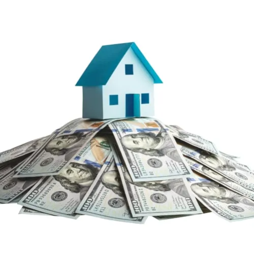 Small blue and white house model sitting atop a pile of US hundred dollar bills on a white background
