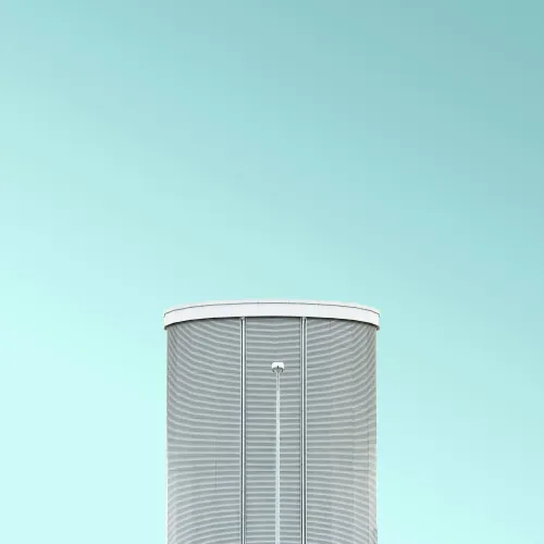 Modern cylindrical building with vertical lines against a clear blue sky, emphasizing minimalist architecture.
