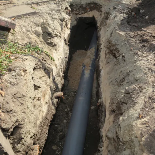 Trench in the ground with a black PVC pipe installed for underground utility or drainage work