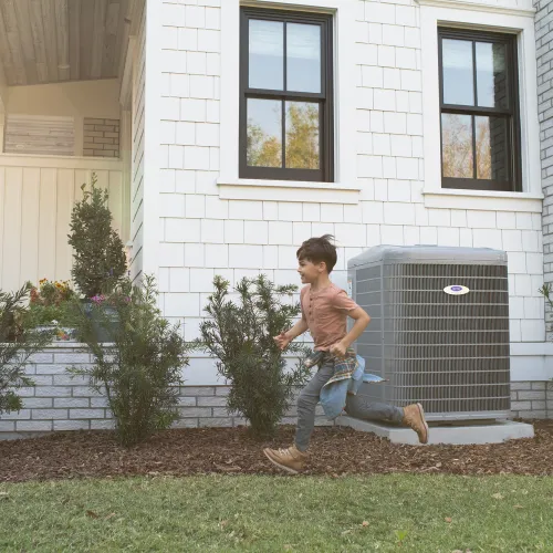Two children running and playing outside a white house with an air conditioning unit against the wall