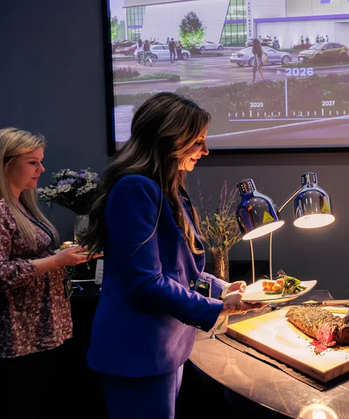 Chef carving roast meat for woman at buffet station during indoor event with digital timeline backdrop.