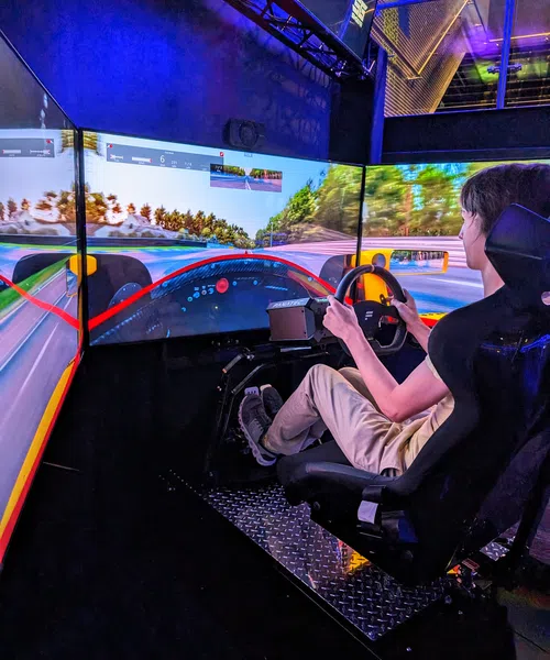 Person racing in a high-tech simulator with immersive screens and realistic steering controls.