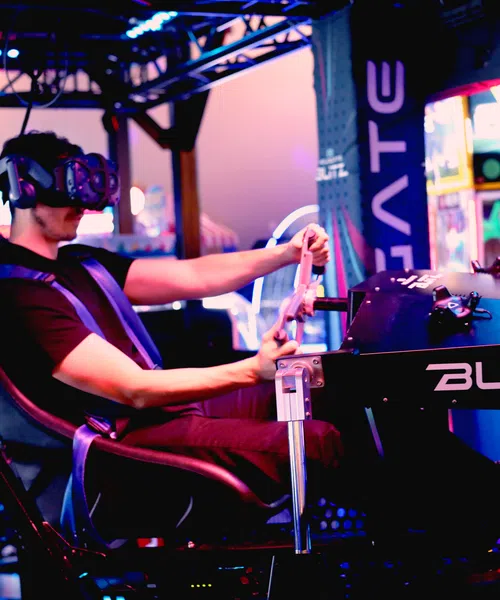 Person racing in a high-tech simulator with immersive screens and realistic steering controls.