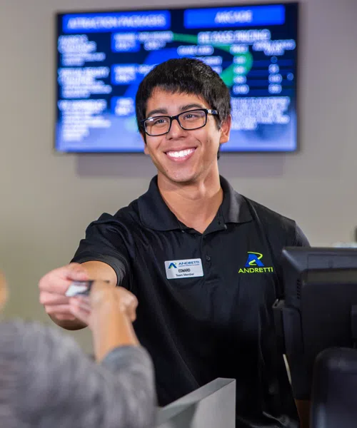 Smiling male customer service employee handing a card to a blonde female client at a counter.