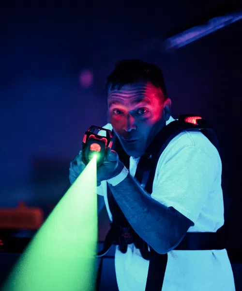 Man playing laser tag in dark room aiming laser gun emitting bright green light beam.