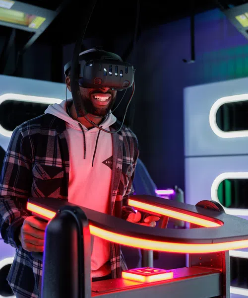 Man enjoying virtual reality gaming experience with VR headset and glowing neon controllers in arcade.